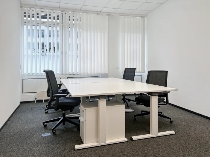 Heller Arbeitsraum mit Schreibtischen, Bürostühlen und großen Fenstern